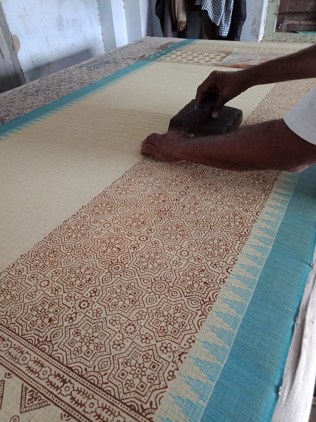 An artisan hand block printing a long length of fabric