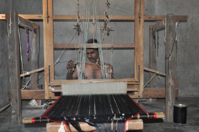 A Kutch weaver working at a traditional pit loom, with the woven fabric in front of him
